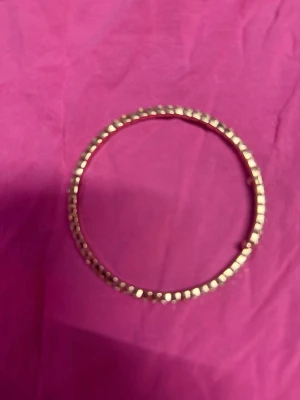 Guldigt armband med pärldetaljer - Snyggt armband i guldfärg med små pärlliknande detaljer runt hela bandet. Armbandet är runt och har en stilren, glittrig look som passar perfekt till din outfit. Materialet ser ut att vara metall med pärldekor.