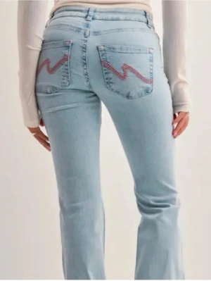 Ljusblå bootcut jeans med slitningar - Säljer ett par ljusblå bootcut jeans med slitningar över knäna och broderade detaljer i rosa på bakfickorna. Tyvärr är dom lite söndertrampade längst ner på byxbenen då dom är för långa för mig💞