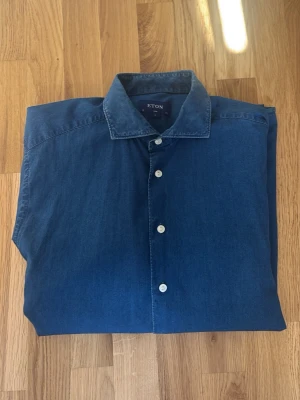 Blå skjorta från Eton i bomull - Snygg blå skjorta från Eton i mjuk bomull. Klassisk krage, vita knappar och lång ärm. Perfekt till jeans eller chinos för en clean och stilren look. Pris kan diskuteras 