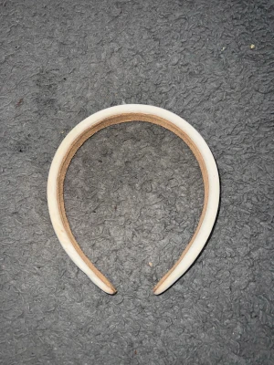 Vitt brett diadem i plast - Säljer ett stilrent vitt diadem med bred form. Diademet är gjort i plast och har en enkel, clean look som passar till många olika outfits. Insidan är beige och ger en skön känsla mot håret. Perfekt accessoar för att lyfta din stil.