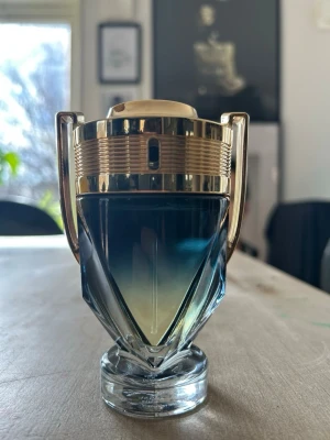 Paco Rabanne Invictus parfym 100 ml - Snygg parfymflaska från Paco Rabanne i form av en pokal med guldfärgade detaljer och transparent glas. Flaskan har en modern och sportig design som verkligen sticker ut på hyllan. Perfekt för dig som gillar exklusiva och unika dofter.