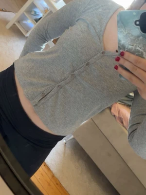 Grå ribbad cardigan med knappar - Snygg grå cardigan med ribbad känsla och v-ringning. Tröjan har långa ärmar och knappar hela vägen framtill, perfekt att bära öppen eller stängd. Enkel och stilren design som passar till det mesta.