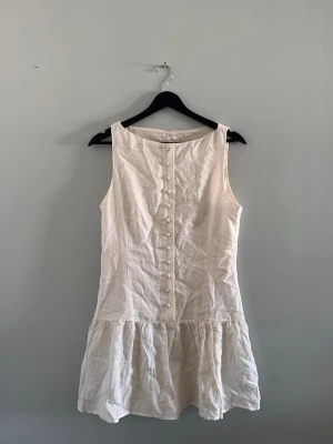 Vit ärmlös kortklänning med knappar - Söt vit kortklänning i linne med volang nedtill, perfekt till studenten och sommaren🌸 Helt ny och endast testad med lappen kvar☺️