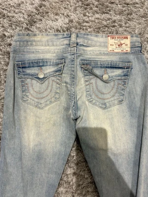 Ljusblå bootcut jeans True Religion - Köpta från true religion i Kanada.True religion:  Midja: 40 cm Innerbenslängd: 78,5 cm . OBS liten defekt längst nere vid benen, se sista bilden.