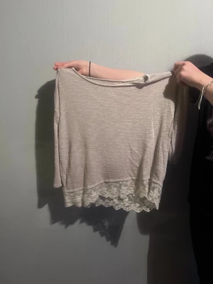 Beige topp med spetskant - Söt beige topp med lång ärm och bred spetskant längst ner. Toppen har en lös passform och är perfekt för en chill och avslappnad stil. Materialet känns mjukt och lätt, och spetsdetaljen ger en extra touch.