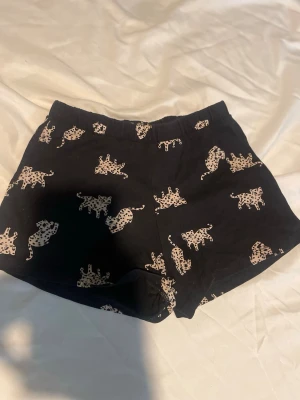 Svarta shorts med leopardmönster H&M barn st 122 - Säljer ett par svarta shorts från H&M med beige leopardmönster. Shortsen har resår i midjan och är gjorda i mjukt bomullstyg. Barn storlek 122