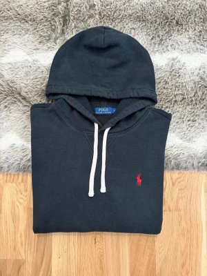 Svart Polo Ralph Lauren Hoodie - Storlek M - Hej! 👋 Säljer en riktigt snygg och stilren svart Polo Ralph Lauren hoodie i storlek M. Den har den ikoniska pony-loggan broderad i rött på bröstet – en klockren färgkombo! 🐎 Tröjan är i mycket gott skick, djupsvart i färgen och har den mjuka fleece-insidan kvar ✨ Sitter perfekt (Modell: 177cm) 👕 Modellen saknar QR-kod, men alla invändiga tvättlappar sitter kvar för att intyga äktheten ✅ Ett perfekt basplagg av hög kvalitet som håller länge. Fraktar snabbt! 🚛📦💬💯 