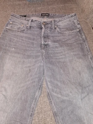 Grå raka jeans från Jack & Jones - Säljer ett par grå jeans från Jack & Jones med rak passform och klassisk femficksdesign. Jeansen har en ljus tvätt och är tillverkade i denim. Perfekta för en avslappnad och trendig look.