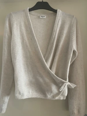 Beige omlottkofta från Kappahl - Säljer en mjuk beige stickad omlottkofta i storlek 170 men passar som xs/s från Kappahl med knytband i sidan. Koftan har lång ärm och ribbade kanter. Perfekt att slänga över en topp för en chill look.