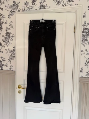 Svarta utsvängda jeans från 157 - Säljer ett par svarta jeans från 157 med hög midja och utsvängda ben. Klassisk femficksmodell med knapp och dragkedja framtill. Jeansen är i ett stretchigt denimtyg som sitter snyggt och bekvämt. är i storlek XS Short.