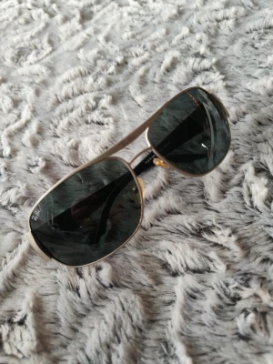 Ray-Ban pilotbågar i silver och svart - Snygga Ray-Ban solglasögon med klassisk pilotform. Bågarna är i silvrigt metall och glasen är mörkt tonade i svart. Tidlös design med tunna skalmar och näskuddar för extra komfort. Perfekta för dig som vill ha en ikonisk och stilren look.