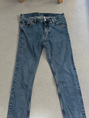 Blåa slimfit jeans från weekday splitternya - Säljer ett par blå jeans med rak passform och hög midja. Jeansen har fem fickor, knappgylf och klassisk denimlook. Materialet är kraftig bomullsdenim och färgen är mellanblå med lätt tvättad effekt. Perfekta till en avslappnad stil.