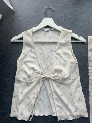 Blommig ärmlös linnetopp med knyt - Supersöt topp med lite struktur med blommigt mönster. Köpt från Lager 157 och i storlek XS. Kanske använd en gång! Perfekt för våren och sommaren☺️