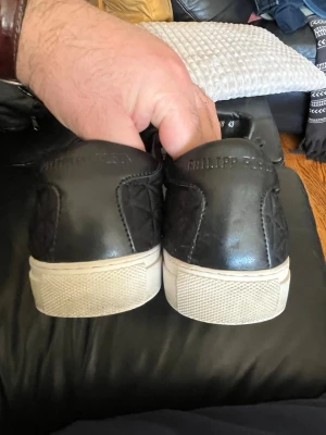 Svarta quiltade sneakers Philipp Plein - Snygga svarta sneakers från Philipp Plein med quiltat mönster och metallplatta på plösen. Skorna har svarta skosnören och vit sula. Limited Edition-design som sticker ut med exklusiva detaljer och modern look.