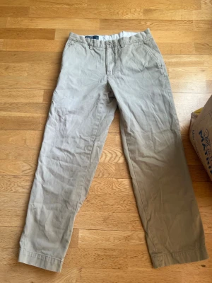Beige chinos från Polo Ralph Lauren - Snygga beige chinos från Polo Ralph Lauren med klassisk rak passform och diskret knappstängning. Tillverkade i 100% bomull för en skön och luftig känsla. Perfekta för dig som gillar stilrena och tidlösa plagg.