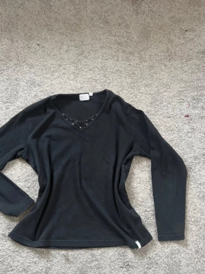 Svart långärmad topp med paljettdetalj - Svart långärmad topp från Gina Tricot med v-ringning och dekorativ spetskant med svarta paljetter vid halsen. Tillverkad i mjukt material som känns skönt mot huden. Perfekt för dig som gillar enkla men snygga detaljer.