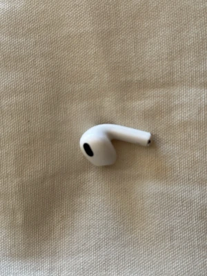 Vit trådlös earbud från Apple - Säljer en vit trådlös earbud från Apple, klassisk AirPods-design med rundad form och svart detalj på högtalaren. Tillverkad i blank plast och passar perfekt för dig som vill ha smidig musikupplevelse utan sladdar.