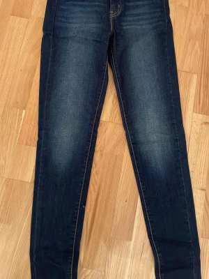 Mörkblå skinny jeans från Levi's - Snygga mörkblå skinny jeans från Levi's med klassiska kontrastsömmar och femficksmodell. Jeansen har en lätt tvättad look framtill och bakfickor med den ikoniska Levi's-sömmen. Perfekta för en trendig och avslappnad stil.