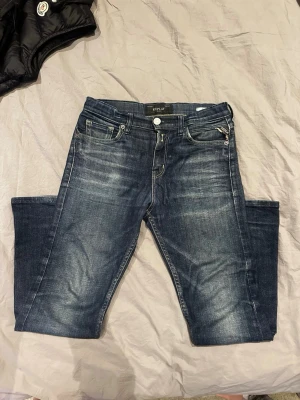 Mörkblå Replay jeans med slitningar - Snygga mörkblå jeans från Replay med slitna detaljer och klassisk femficksmodell. Jeansen har en rak passform, tydliga kontrastsömmar och Replay-lapp bak i midjan. Tillverkade i denim med cool tvätt och dragkedja i gylfen.
