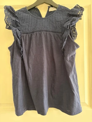 Blå ärmlös topp med volang - Supersöt blå ärmlös topp från Odd Molly med volangdetaljer och broderade spetsärmar. Överdelen har ribbad struktur och dekorativ kant. 