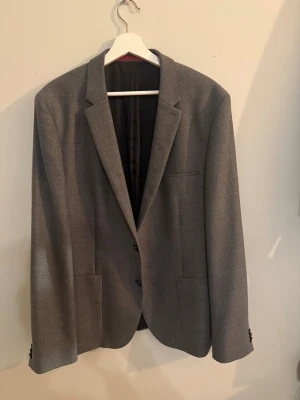 HUGO (Hugo Boss) kavaj – grå – strl 54 - Stilren kavaj från HUGO (Hugo Boss) i en elegant grå nyans. Modern passform med rena linjer.  Tillverkad i ett lätt och bekvämt material med fin struktur och exklusiva detaljer invändigt.   Kavajen är i gott skick med normalt bruksslitage.  Storlek: 54 (motsvarar ca L/XL) Färg: Grå Skick: 8/10  📦 Kan skickas 💬 Kontakta vid frågor eller intresse