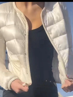 Vit dunväst med dragkedja - Snygg vit dunväst med quiltad design och dragkedja framtill. Västen har rundad halsringning och diskreta fickor på sidorna. Perfekt att slänga över en hoodie eller tröja för extra värme. Lätt och smidig att bära, passar till många olika stilar.