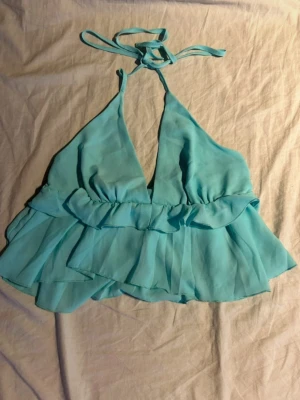 Turkos topp med knyt i nacken - Somrig turkos linnetopp med volanger och knytning i nacken 💙 Djup v-ringning och luftig passform som känns lätt och sval mot huden. En riktig sommarfavorit till shorts, kjol eller linnebyxor.(ifrån shein) 