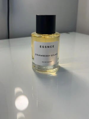 ESSNCE Strawberry Eclair parfym - ESSNCE Strawberry Eclair Eau de Parfum i en stilren, cylindrisk glasflaska med svart lock. Parfymen har en ljusgul vätska och etiketten är enkel och modern. Doften har troligen söta och fruktiga toner av jordgubb.