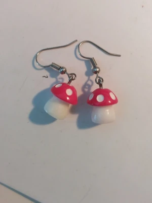 Svampar i akryl örhängen - Säljer ett par örhängen formade som små röda och vita flugsvampar. De är gjorda i akrylplast med metallkrokar. Perfekt för dig som gillar lekfulla och färgglada accessoarer med unik design.