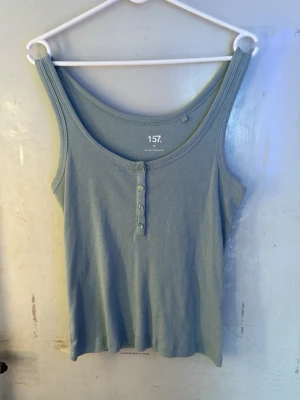 Ribbad linnetopp  - Två ribbade linnetoppar , en i ljusgrön och en i mörkblå färg. Båda har rund halsringning och dekorativa knappar framtill. Perfekta för sommaren och lätta att matcha med olika outfits. (Båda för 50 kr)