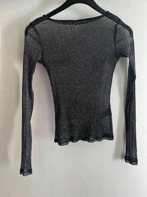 Svart glittrig mesh topp från Nelly - Snygg svart mesh topp från Nelly i storlek XS. Toppen har lång ärm och är tillverkad i ett glittrigt, tunt material som ger en cool och trendig look. Perfekt att styla lager på lager eller bära som statement piece. Ursnygg som festtopp med t.ex en snygg bh under men känner mig inte bekväm i den tyvärr. Endast testat men lappen är borttagen.