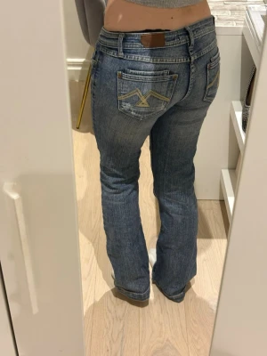 Blå bootcut jeans med broderade fickor - Säljer ett par blå bootcut jeans med snygga broderade detaljer på bakfickorna och klassisk läderpatch i midjan. Jeansen har normalhög midja och är tillverkade i slitstarkt denimtyg. Perfekta för en avslappnad och trendig look.