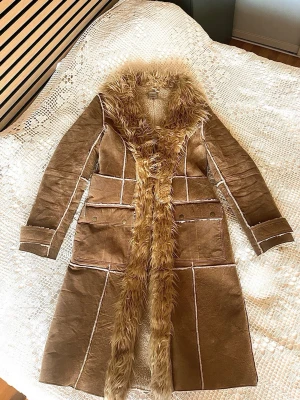 Brun fuskpälsfodrad kappa Vero Moda - Säljer en brun lång kappa från Vero Moda med fuskpäls längs krage och framkant. Kappan har markerade sömmar, stora fickor och är fodrad med mjuk teddy på insidan. Perfekt för dig som vill ha en retro och trendig look i höst och vinter.