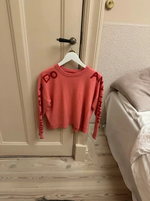 Rosa stickad Zadig tröja - Trendig rosa stickad tröja med mörkare rosa texten 'GIRLS CAN DO ANYTHING' längs halsringningen och ena ärmen. Tröjan har en klassisk passform och rund hals. Perfekt för dig som vill ha ett statement-plagg i garderoben.