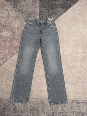 Grå straight jeans från Stradivarius - Snygga grå straight jeans från Stradivarius med klassisk femficksdesign och hög midja. Jeansen har raka ben och är tillverkade i denim med en cool tvättad look. Perfekta för dig som gillar en avslappnad och trendig stil.