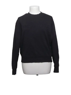 Svart sweatshirt med broderad text Carin Wester  - En svart sweatshirt med diskret broderad text över bröstet. Tröjan har rund halsringning, långa ärmar och ribbade muddar vid ärmslut och nederkant. Perfekt för en avslappnad och stilren look.