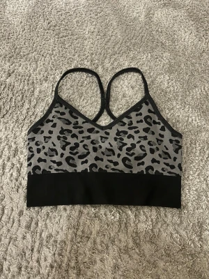 Grå leopardmönstrad sporttopp - Snygg sport-bh från Stronger i grått med svart leopardmönster och tunna axelband som korsas i ryggen. Storlek M/L men passar även S. Aldrig använd! ❣️❣️