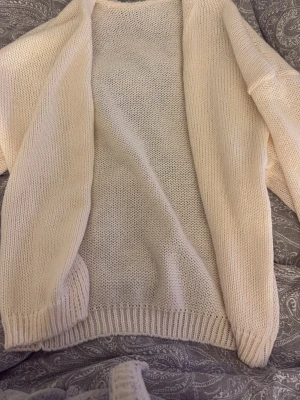 Krämvit stickad cardigan - Mysig krämvit stickad cardigan med öppen front och långa ärmar. Tröjan har ribbstickade muddar vid ärmslut och nederkant. Perfekt att slänga över en t-shirt för en chill look. Materialet känns mjukt och följsamt.