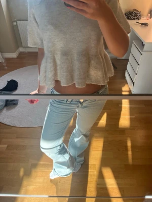 Ljusbeige stickad topp med volang - Superfin ljus beige stickad topp med korta ärmar och volang nedtill. Toppen har en croppad passform och rund halsringning. Perfekt att styla med jeans eller kjol för en trendig look.