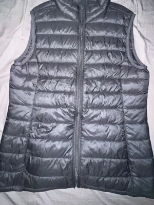 Svarta vest jacka Whistler - svart dunväst från Whistler med hög krage och dragkedja framtill. Västen har quiltad design med horisontella sömmar och två sidofickor. Perfekt för lager-på-lager och håller dig varm under kyliga dagar.
