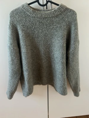 Grå/grön stickad tröja  - Grå/grön stickad tröja med rund halsringning och långa ärmar. Tröjan kan upplevas lite stickig men inte så farligt. Använder inte längre då den är för kort i armarna.