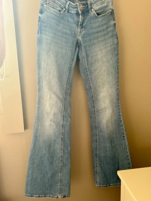 Blå bootcut jeans med utsvängda ben - Säljer ett par ljusblå bootcut jeans med klassisk femficksmodell och utsvängda ben. Jeansen har normal midja och är tillverkade i denim med lätt tvättad look. Perfekta för dig som gillar retrostil och vill ha ett par bekväma jeans med snygg passform.