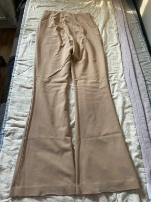 Beige utsvängda leggings - Säljer ett par beige leggings med utsvängda ben och hög midja. Materialet är mjukt och stretchigt, vilket gör dem riktigt bekväma. Perfekta att styla med en oversized hoodie eller crop top för en chill look.