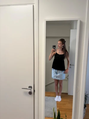 Svart glittrig linnetopp från Gina  - Snygg svart linnetopp med tunna axelband och glittriga detaljer framtill. Toppen har en rak passform och är perfekt för dig som vill ha något enkelt men ändå extra. Passar till både jeans och kjol.