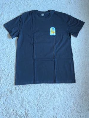 Svart t-shirt med färgglatt tryck - Säljer en svart t-shirt med ett färgglatt grafiskt tryck fram och stort tryck bak med texten 'Casa Blanca'. T-shirten har klassisk passform och är kortärmad. Perfekt för dig som gillar stilrena plagg med en twist.