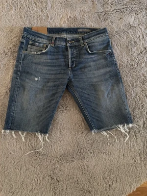 Dondup jeans som har gjorts till jeansshorts Blå med rå kant - Säljer ett par blå dondup jeansshorts med klassisk femficksmodell och slitna, råa kanter nedtill. Shortsen har normal passform och är tillverkade i bomull. Perfekta för en avslappnad stil under varmare dagar.