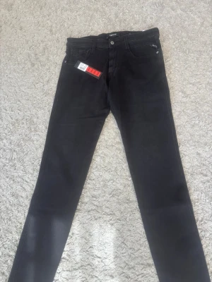 Svarta skinny jeans från Replay - Säljer ett par svarta skinny jeans från Replay med klassisk femficksdesign och diskreta detaljer. Jeansen har en smal passform och är tillverkade i stretchigt material för extra komfort. Perfekta för en trendig och avslappnad stil.