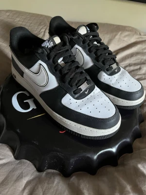Nike Air Force 1 pandas sneakers - Säljer ett par klassiska Nike Air Force 1 sneakers i svart och vitt. Skorna har en låg silhuett, svart ovandel med vita detaljer och perforerad tåbox för extra ventilation. Ikonisk Swoosh-logga på sidan och Nike Air-märkning på plösen. Skorna är i ett använt skick och säljes då de ej passar mig längre.