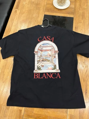 Svart CasaBlanca t-shirt - Snygg svart t-shirt från Casa Blanca med stort tryck på ryggen och mindre tryck på bröstet. Motivet visar en klassisk båge med landskap och texten 'Casa Blanca' i rött. Perfekt för dig som vill sticka ut med stilren design.