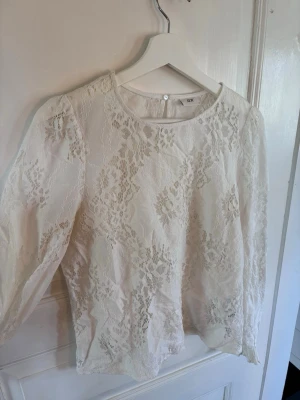 Vit spetsblus från JDY - Superfin vit blus i spets från JDY med rund halsringning och långa ärmar. Blusen har ett vackert blommigt spetsmönster och knäppning bak i nacken. Perfekt att styla med jeans eller kjol för en fräsch look.